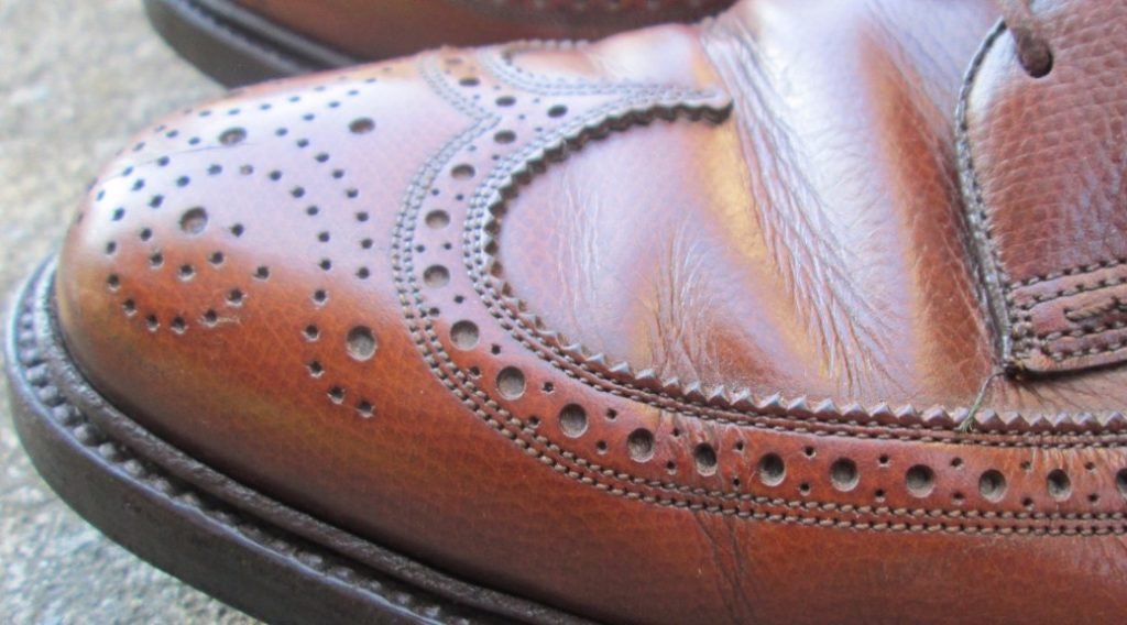 Close-up of polished brogue leather shoe highlighting craftsmanship and detailed leather finishing.